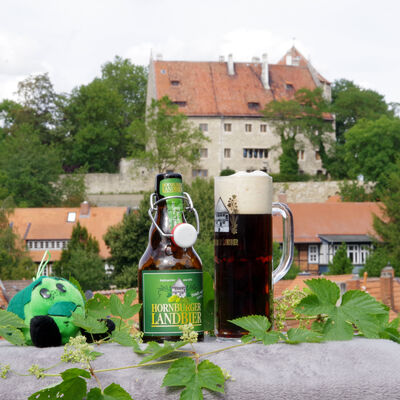 Bild vergrößern: Vor dem malerischen Hintergrund der Hornburg steht im Vordergrund die regionale Spezialität "das Hornburger Landbier"